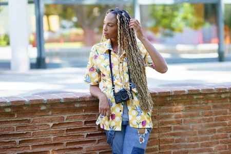 African influencer combed with colorful braids standing with a camera outdoors