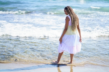 Black female walking along the shore of the beach wearing a beautiful long dress