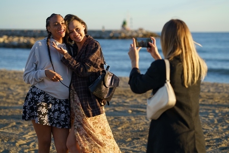 Faceless woman photographing cheerful diverse girlfriends on seashore