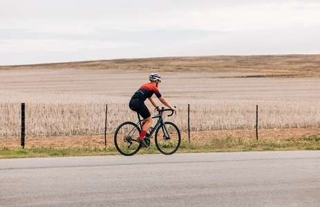 Side view of professional female cyclist riding pro bike against agriculture field