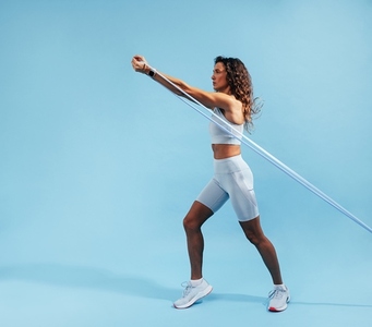 Side view of muscular woman exercsing with elastic band on blue background  Slim female in sportswear working out in studio