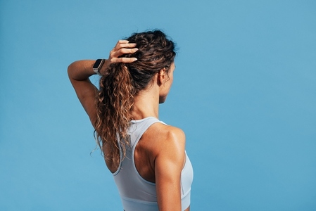 Back view of a muscular woman adjusting her hair while standing on blue background