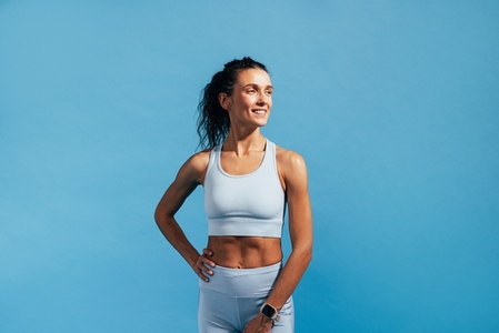 Smiling woman in fitness wear standing on blue background and looking away