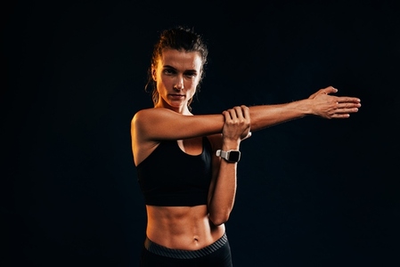 Female athlete in sportswear doing warm up exercise on black background