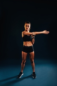 Full length on young woman in fitness wear warming up her hand on black background