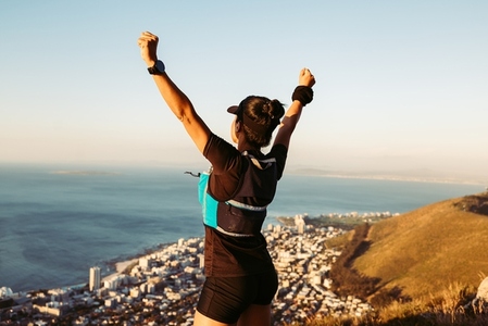 Side view of female runner with arms outstretched on mountain peak at sunset
