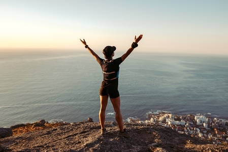 Rear view of fit woman standing on mountain top looking at view with arms wide open