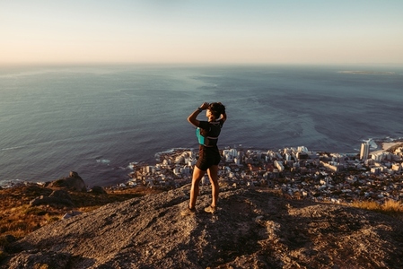 Woman in sportswear standing on the cliff and looking at the view at sunset  Female trail runner relaxing on mountain top looking at the ocean