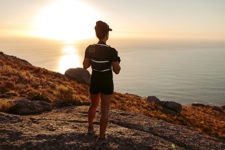 Rear view of a woman in sports clothes looking at the ocean  Young female standing on a mountain trail enjoying the view