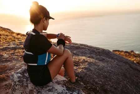 Woman hiker sitting on a rock on the top of the mountain checking smartwatch  Female in sportswear on a hill at sunset