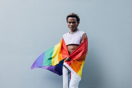 Man with a pride flag posing on grey background outdoors