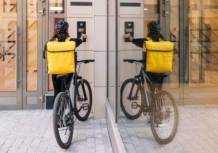 Rear view of a woman courier with backpack using an apartment intercom for delivery