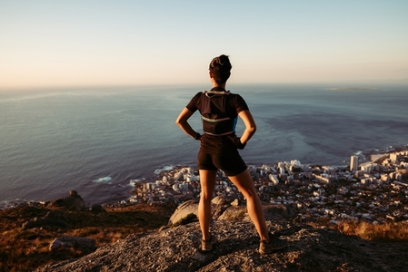 Rear view of sportswoman enjoying the view from the top  Female runner in sportswear taking a break on a hill at sunset