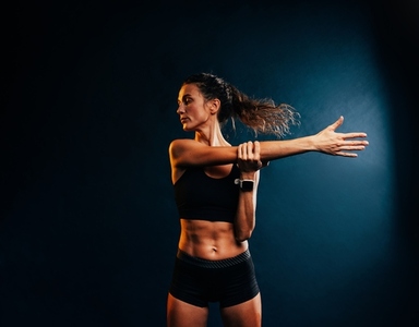Muscular woman doing intense training warming up her hands on black background