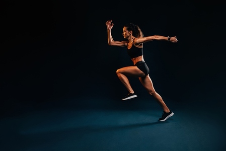 Muscular healthy woman running  Caucasian female runner in sportswear sprinting on black background