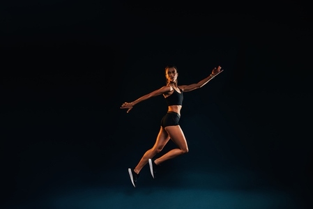 Slim woman working out on black background  Female athlete doing jumps in studio
