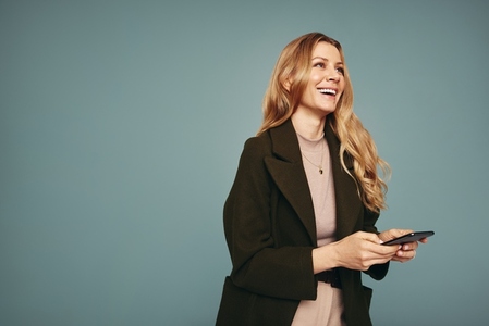 Smiling blonde woman holding a smartphone in a studio