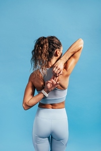 Back view of fitness woman stretching her hands against blue background  warming up