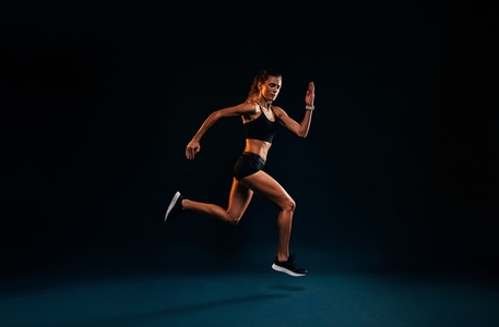 Female runner sprinting on black background  Fit woman jumping while exercising in studio