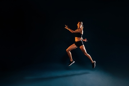 Runner in sports clothes jumping  Woman sprinting on black background