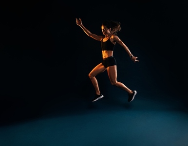 Slim woman in sportswear doing jumps on black background