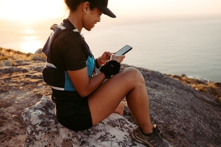 Trail runner holding smartphone while sitting on peak at sunset