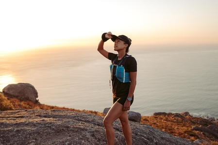 Woman trail runner holding a cap while walking up on a hill
