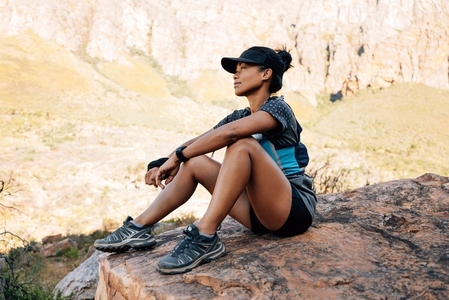 Side view of sportswoman sitting on a rock and relaxing  Young female hiker taking a break during exercises enjoying the view
