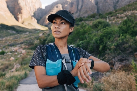 Portrait of healthy trail runner checking smart watch  Woman in sportswear taking a break during hike looking away