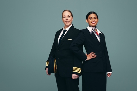 Happy airline captain and air hostess smiling in a studio