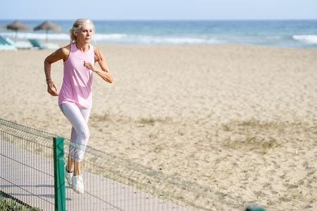 Older female doing sport to keep fit  Mature woman running along the shore of the beach