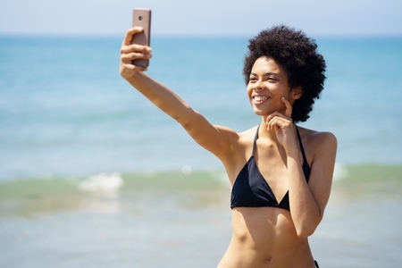 African American woman with afro hairstyle taking a selfie with her smartphone on a tropical beach