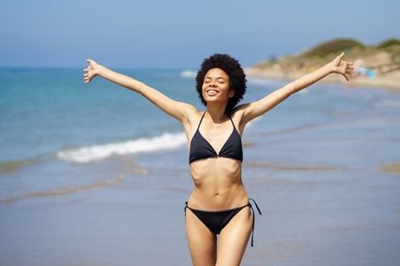 Cute black woman opening her arms on the beach to enjoy her holiday in the sun