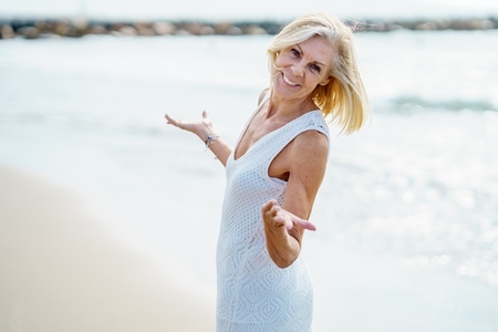 Smiling mature woman walking on the beach  spending her leisure time  enjoying her free time