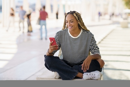 Black female using a smartphone sitting on a bench outdoors  wearing her hair in braids