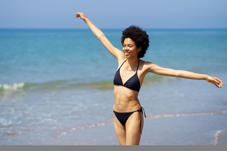 Happy black woman opening her arms on the beach to enjoy her holiday in the sun