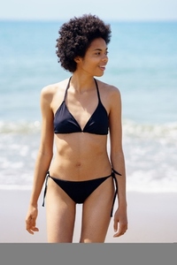 Positive black woman in bikini walking on the beach smiling