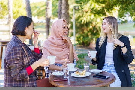 Joyful multiracial women chatting on terrace of cafe