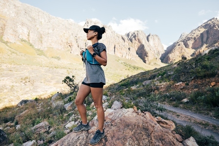 Side view of trail runner in sports wear standing in valley  Young female in fitness attire in wild terrain