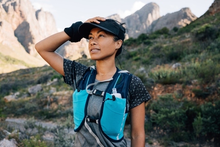 Woman in hiking attire holding cap while standing in valley between mountains