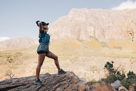 Side view of fit woman standing on a rock enjoying the view against mountains