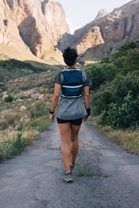 Back view of woman hiker walking on abandoned road in valley  Female exploring new path in wild terrain