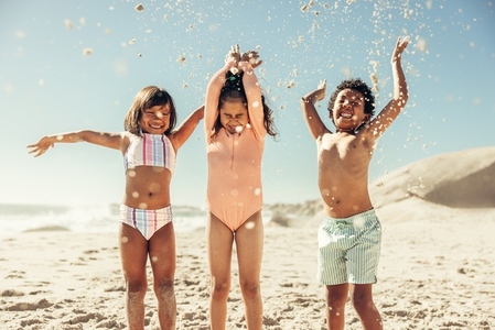 Adorable little kids throwing beach sand into the air