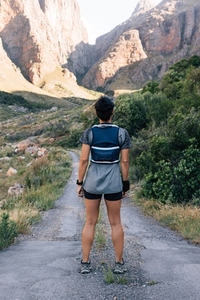 Back view of young healthy hiker standing on abandoned road and looking on mountains