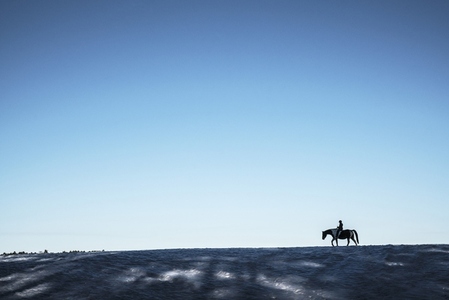 Girl riding Paint Horse in distance on snowy ridge under blue sky