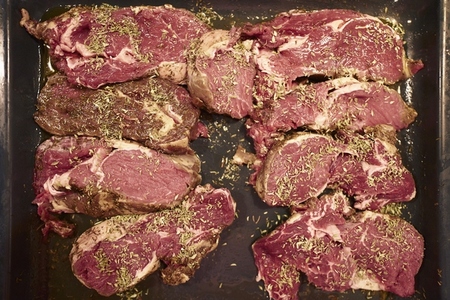View from above raw steaks with seasoning herbs marinating in tray