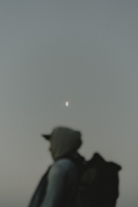 Half moon in sky above male hiker with backpack
