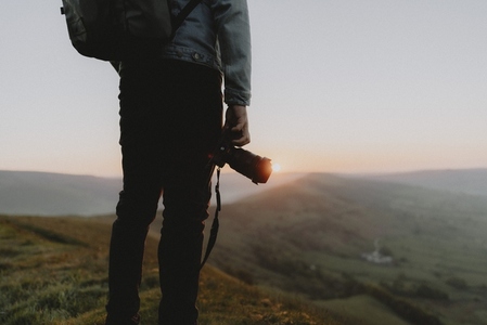 Male photographer with SLR camera on hill overlooking tranquil landscape at sunrise
