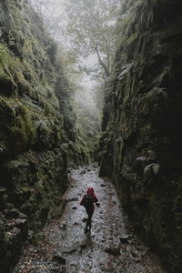 Woman hiking between wet rugged rock walls in forest 1