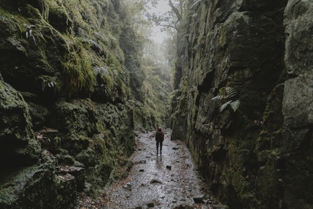 Woman hiking between wet rugged rock walls in forest 2